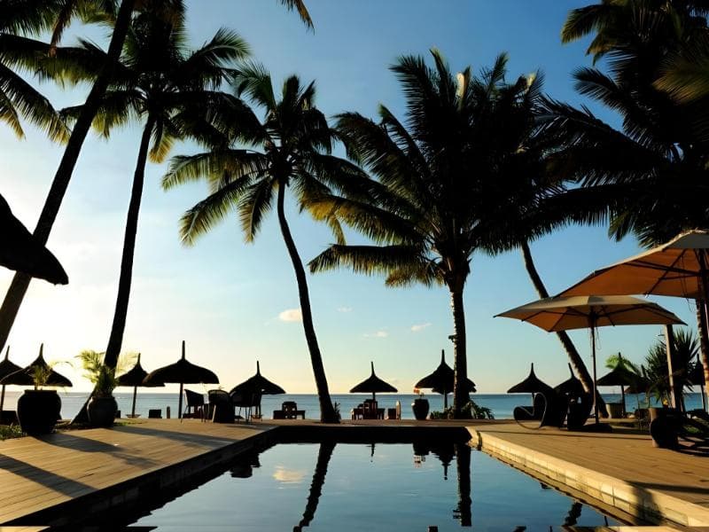 The Sakoa Boutik pool at sunset, coconut palms in silhouette and thatched parasols facing the sea