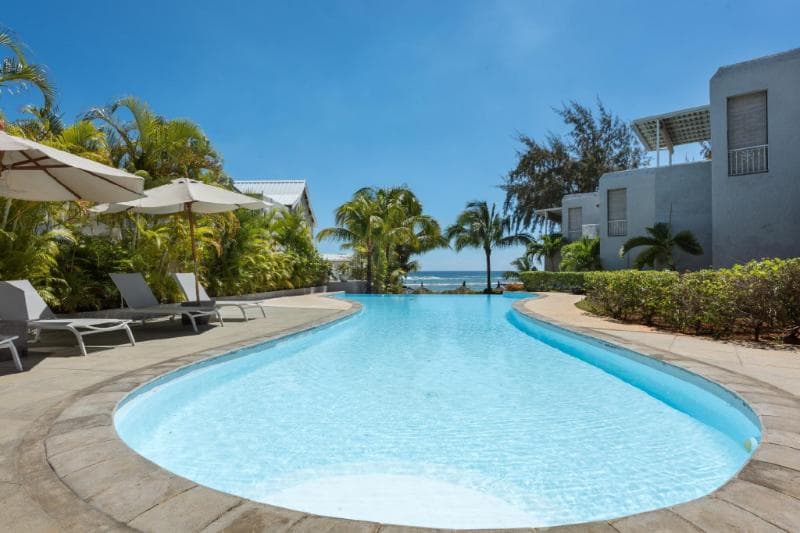 The curved pool at Voile Bleue with loungers, parasols, white buildings and the sea on the horizon