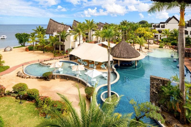 Le Jadis : piscine à paliers et paillotes de chaume devant les bâtiments du resort, mer au loin