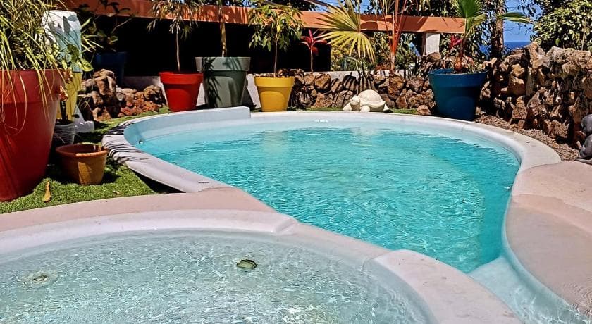 Piscine de La Case aux Sens entourée de pots colorés et d'un muret de pierre, jacuzzi au premier plan