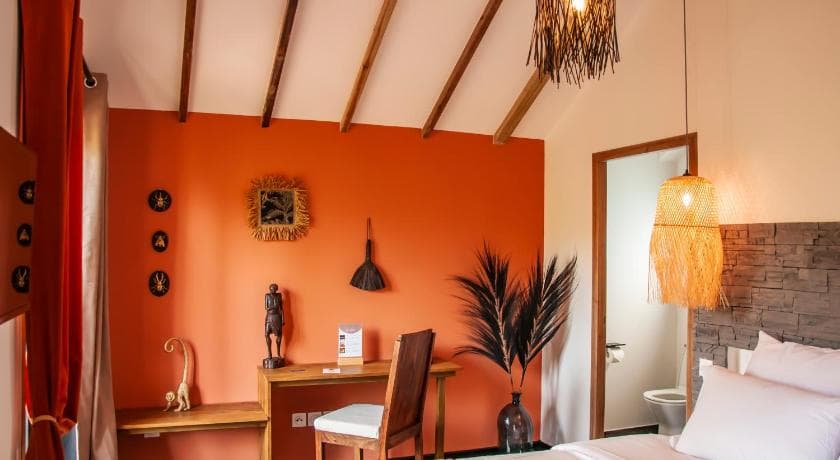 Chambre d'Heritage Ecolodge, mur orange, charpente en bois et bureau décoré d'objets artisanaux