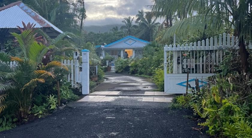 The path at LaKour Fleurie between a white gate and tropical plants, a blue house at the end