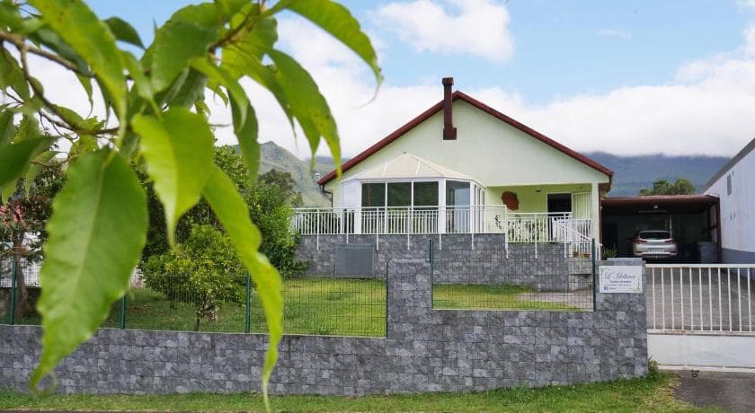 Grande villa blanche de L'Idolivier derrière un muret de pierre, feuillage au premier plan