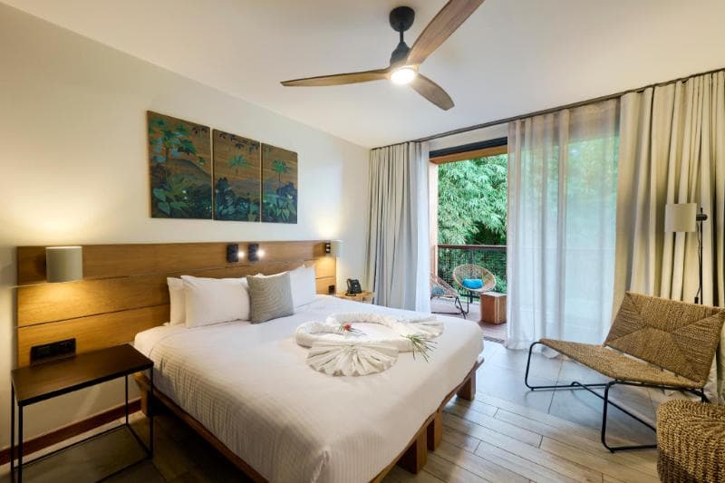 A room at Papangue Hôtel & Spa, white bed, wooden headboard and a glass door onto greenery