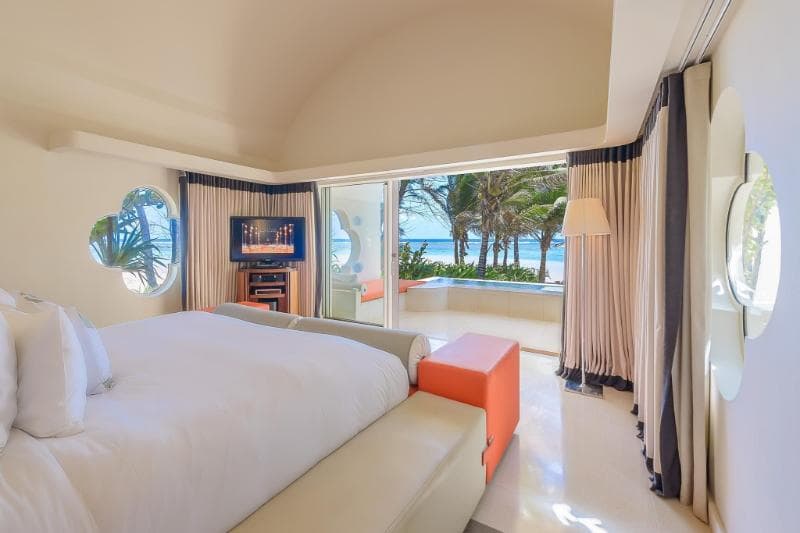Suite du SO Sofitel, lit blanc, fauteuil orange et baie vitrée ouverte sur les palmiers