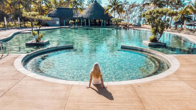 Piscine circulaire de l'Outrigger devant un pavillon au toit de chaume, une cliente assise au bord