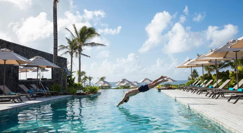 Un nageur plonge dans la piscine bordée de transats et de parasols du Constance Le Chaland IKO