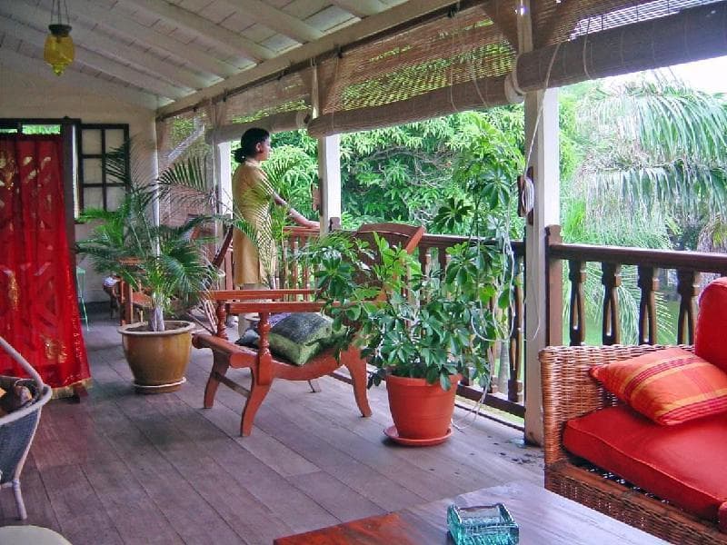Véranda en bois de la maison coloniale du Jardin de Beau Vallon, plantes en pots et fauteuils