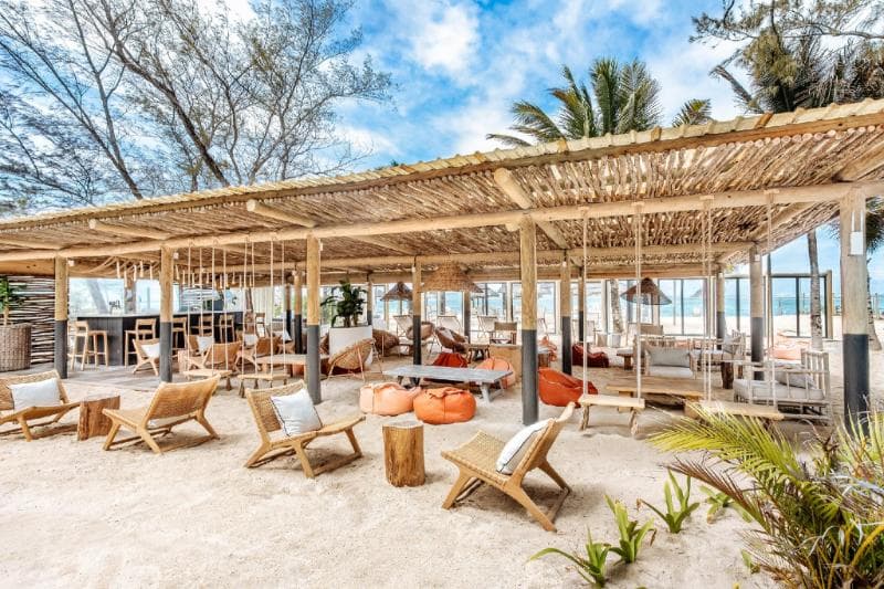 Bar de plage sous une pergola en bois, transats et poufs sur le sable du Friday Attitude