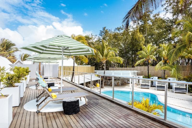 Terrasse en bois avec transats et parasols rayés au bord de la piscine du Tropical Attitude