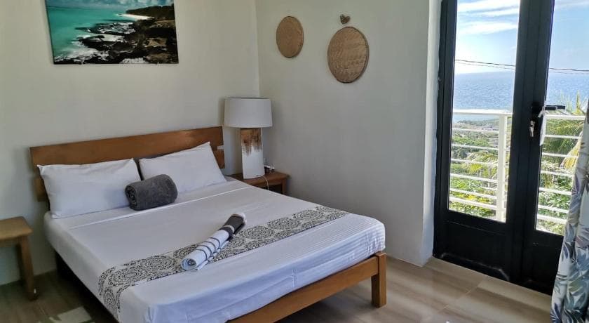 A bright room at Or Saison, with a double bed and a door open onto a sea-view balcony