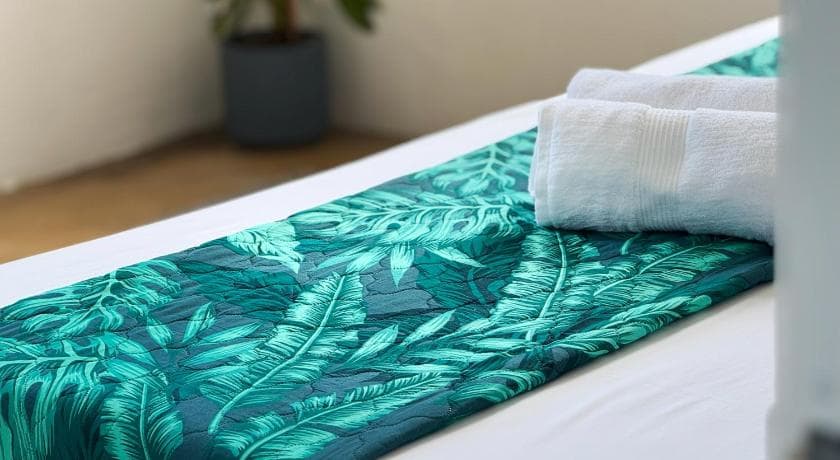 White towels on a leaf-print bed runner at Villa Océan Gravier